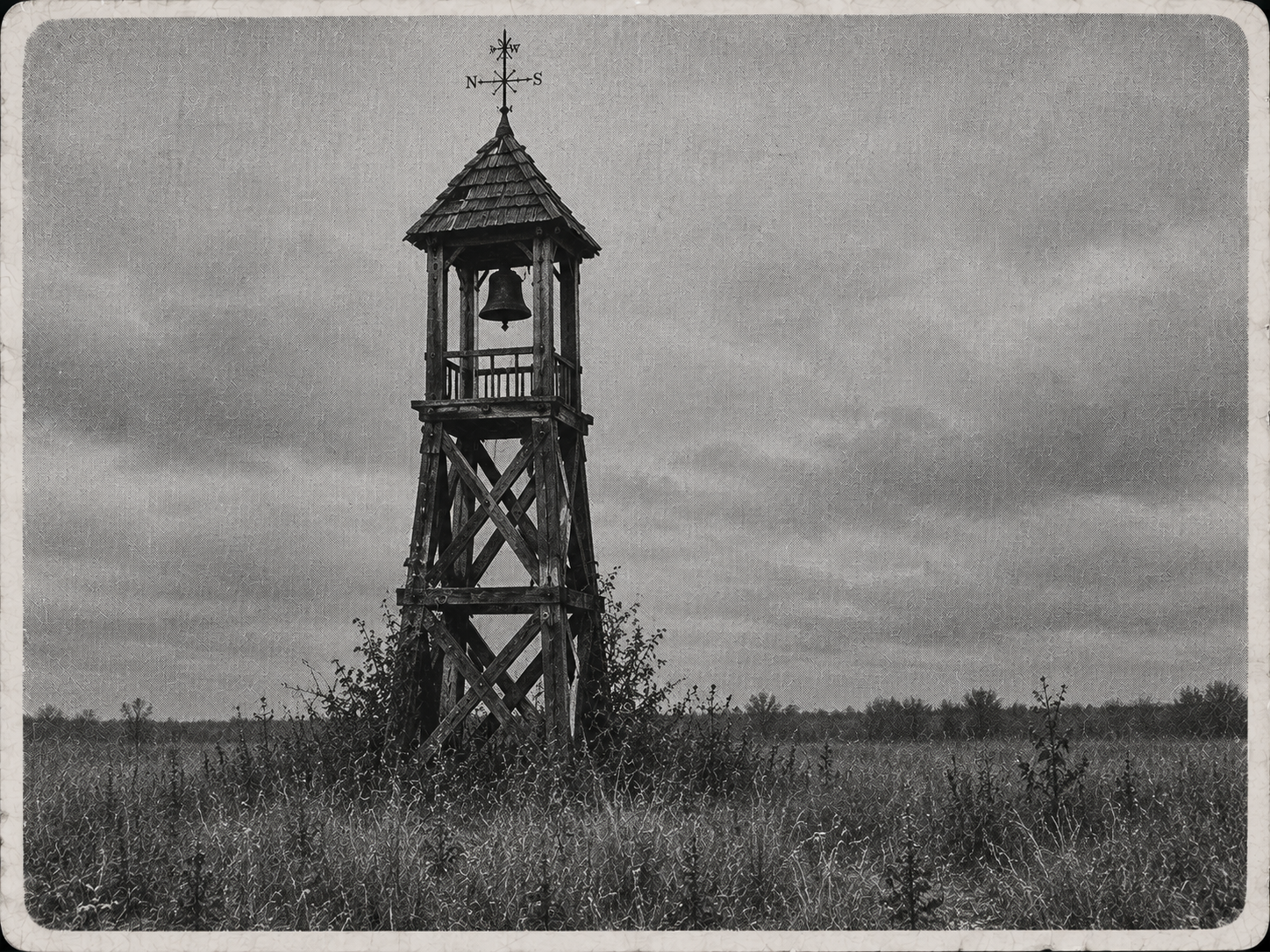 Archival landscape photograph of the weathered wooden bell tower standing alone in an overgrown field.